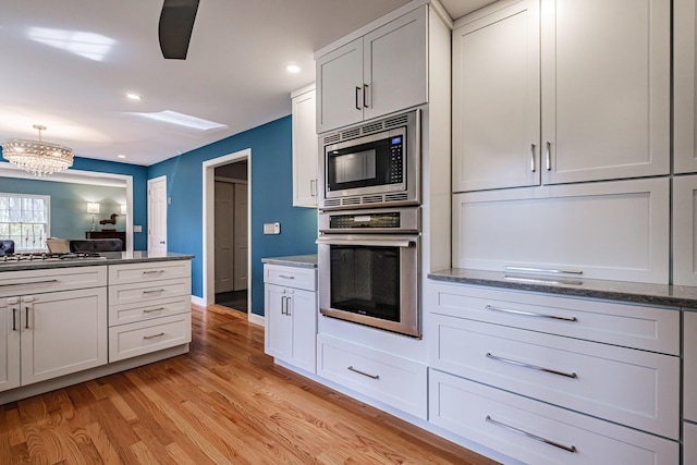kitchen with appliances with stainless steel finishes, a notable chandelier, light wood-style floors, dark stone counters, and recessed lighting