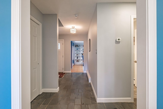 hall with baseboards, a baseboard radiator, and stone finish floor
