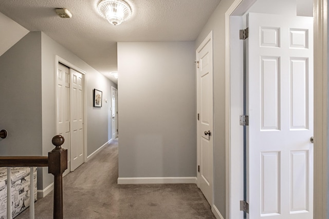 corridor with carpet flooring, a textured ceiling, and baseboards