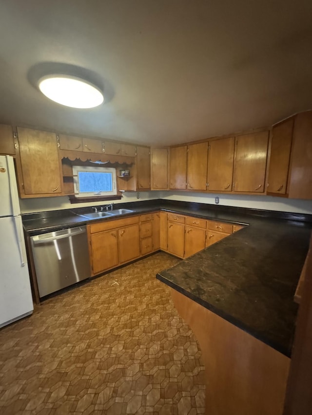 kitchen featuring freestanding refrigerator, dark countertops, a sink, and dishwasher
