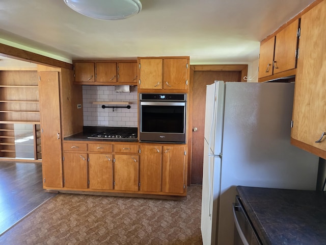 kitchen with freestanding refrigerator, stainless steel oven, decorative backsplash, and brown cabinetry