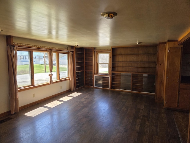 unfurnished living room featuring baseboards, built in shelves, visible vents, and dark wood-type flooring