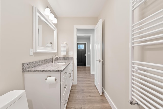 bathroom featuring vanity, toilet, radiator heating unit, baseboards, and wood finished floors