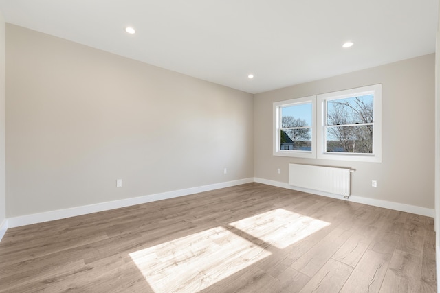 empty room featuring radiator heating unit, baseboards, recessed lighting, and light wood finished floors