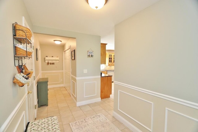 corridor featuring wainscoting, a decorative wall, and light tile patterned flooring