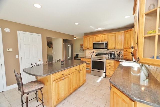 kitchen featuring a kitchen island, appliances with stainless steel finishes, light tile patterned floors, and a breakfast bar area