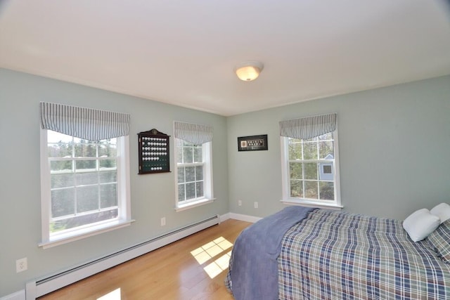 bedroom featuring baseboards, multiple windows, a baseboard heating unit, and wood finished floors