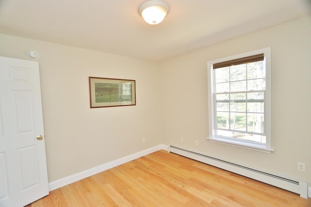 spare room featuring baseboards, a baseboard heating unit, and light wood-style flooring