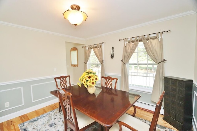 dining area with a wainscoted wall, ornamental molding, light wood-style flooring, and a baseboard radiator