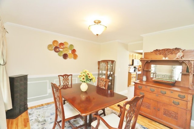 dining room featuring crown molding, light wood finished floors, and wainscoting