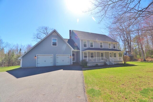 colonial-style house featuring covered porch, a chimney, a front lawn, and aphalt driveway