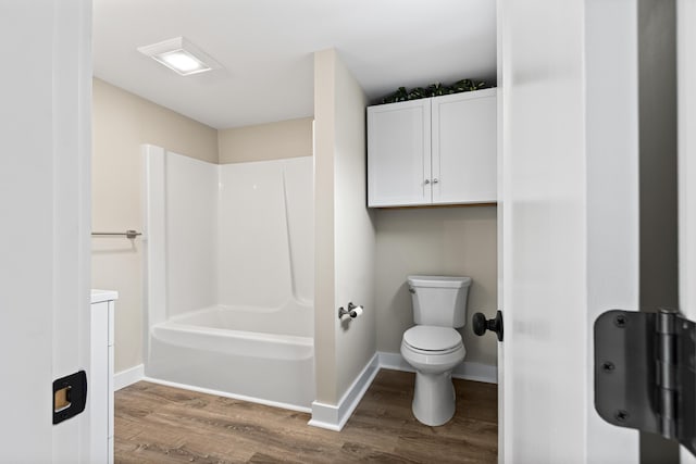 bathroom with baseboards, tub / shower combination, wood finished floors, and toilet