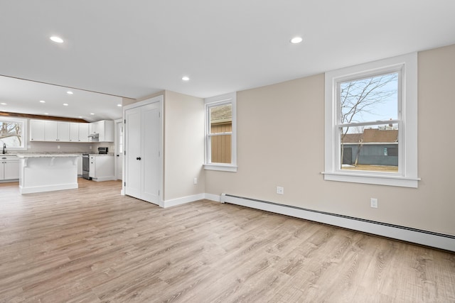 unfurnished living room featuring recessed lighting, a baseboard heating unit, plenty of natural light, and light wood-style flooring