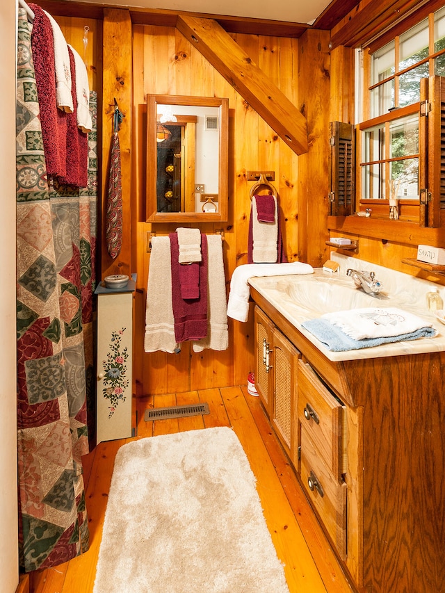 bathroom featuring wood-type flooring, wood walls, visible vents, and vanity