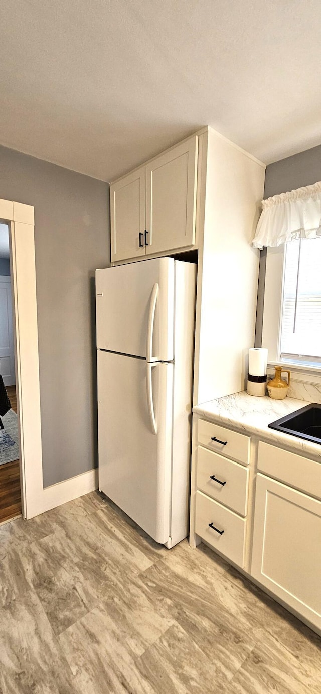 kitchen with freestanding refrigerator, a sink, light stone countertops, and white cabinetry