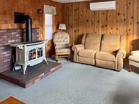 living area with carpet flooring, wooden walls, a wall mounted AC, and a wood stove