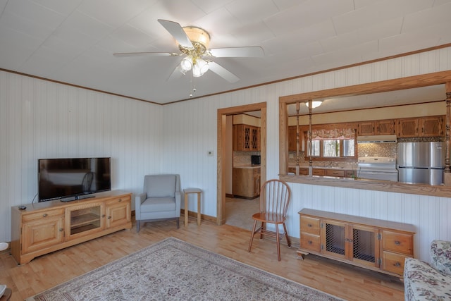 living area with ceiling fan, crown molding, wood walls, baseboards, and light wood-style flooring