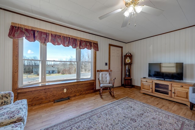 living room featuring ceiling fan, visible vents, wood walls, light wood finished floors, and ornamental molding