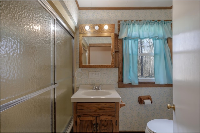 bathroom with toilet, wallpapered walls, a shower with shower door, and vanity
