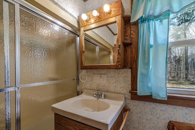 bathroom featuring vanity, a shower with door, and wallpapered walls