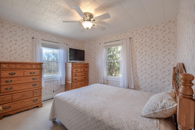carpeted bedroom with wallpapered walls, multiple windows, and ceiling fan