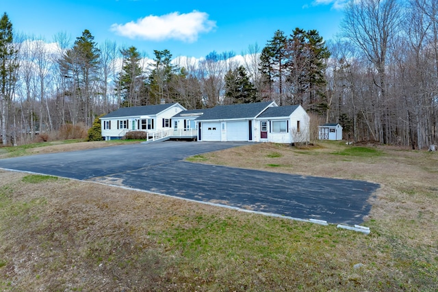 single story home with a storage unit, aphalt driveway, a garage, a front yard, and an outbuilding