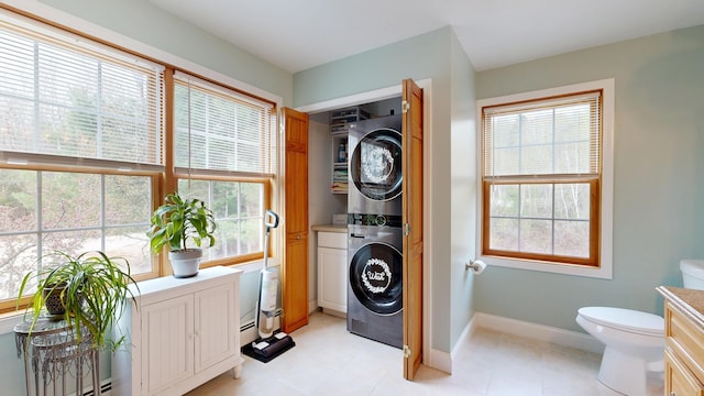 laundry room featuring stacked washing machine and dryer, baseboards, and light tile patterned floors