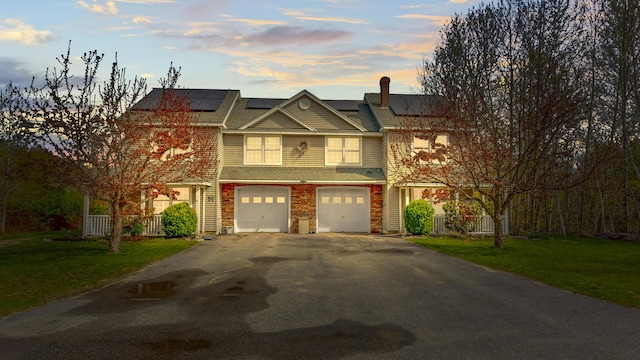 view of front of house featuring asphalt driveway, a front yard, an attached garage, and roof mounted solar panels