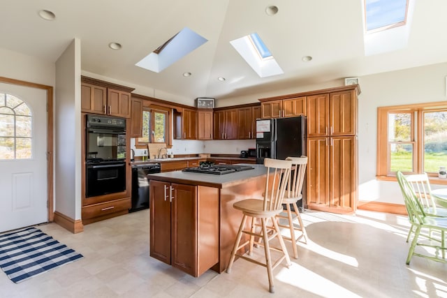 kitchen with brown cabinetry, lofted ceiling with skylight, a breakfast bar area, a center island, and black appliances