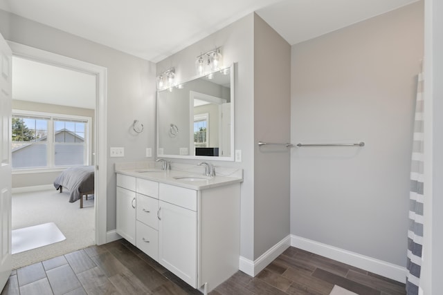 ensuite bathroom with baseboards, double vanity, wood finish floors, and a sink