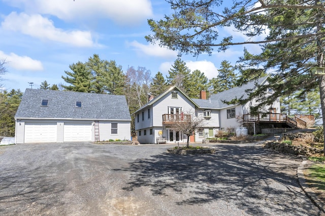 view of front of home featuring a chimney, a wooden deck, a balcony, aphalt driveway, and a shingled roof
