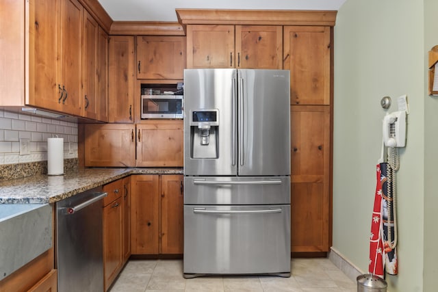 kitchen featuring tasteful backsplash, brown cabinets, light tile patterned floors, dark stone countertops, and stainless steel appliances