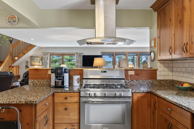 kitchen featuring a healthy amount of sunlight, brown cabinetry, stainless steel range with gas cooktop, and island range hood