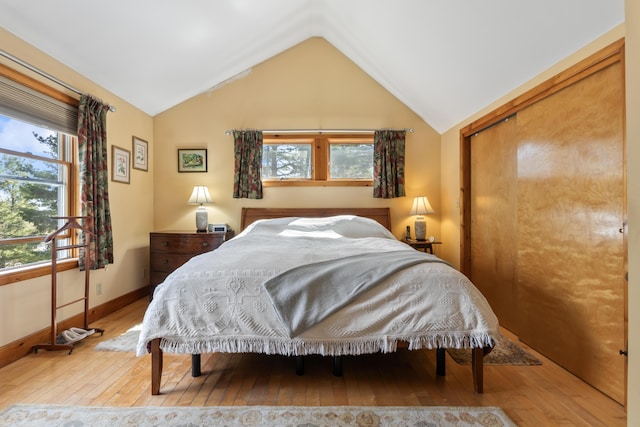 bedroom with a closet, baseboards, lofted ceiling, and hardwood / wood-style floors