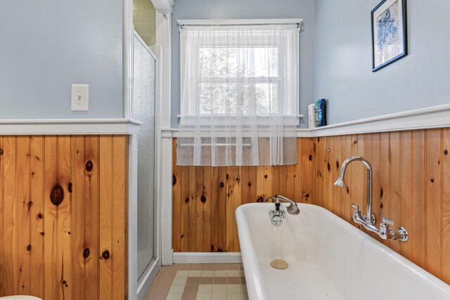 bathroom with a shower with shower door, a soaking tub, and wood walls