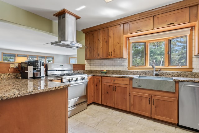 33 Taylor Rd, Westport Island, ME 04578 - kitchen featuring appliances with stainless steel finishes, island range hood, brown cabinetry, light tile patterned flooring, and backsplash