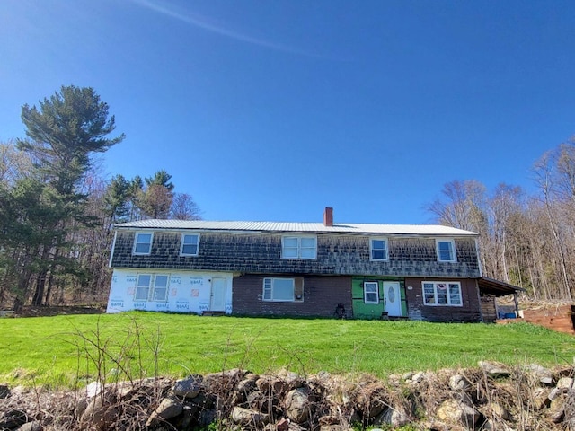 view of front of home featuring a chimney, metal roof, and a front yard