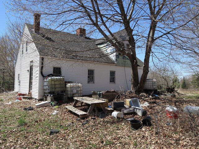 back of house with roof with shingles and a chimney