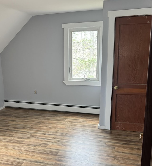 additional living space with a baseboard heating unit, wood finished floors, and vaulted ceiling