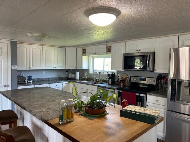 kitchen featuring a kitchen island, a breakfast bar, white cabinetry, a sink, and stainless steel appliances