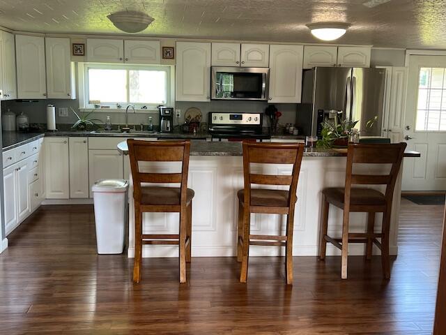 kitchen featuring appliances with stainless steel finishes, a sink, a breakfast bar area, white cabinetry, and dark wood-type flooring