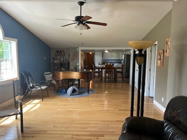 living area with baseboards, ceiling fan, vaulted ceiling, and light wood-type flooring