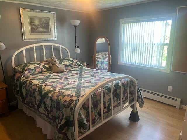 bedroom featuring crown molding, baseboards, wood finished floors, and a baseboard radiator
