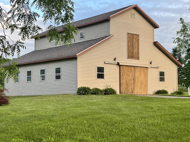 back of house featuring a barn, a shingled roof, a garage, an outbuilding, and a yard