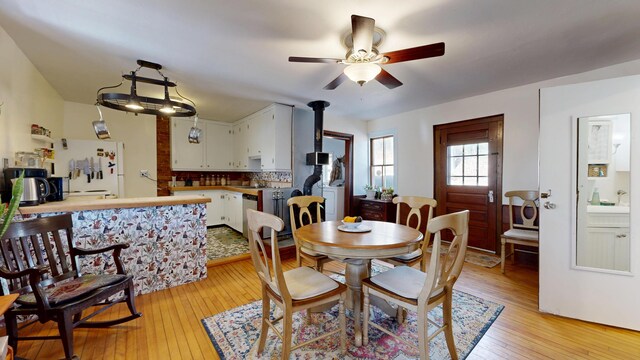 dining room with light wood-style floors, a wood stove, and ceiling fan