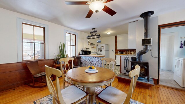 dining space featuring washer / dryer, a ceiling fan, a wood stove, and light wood-style flooring