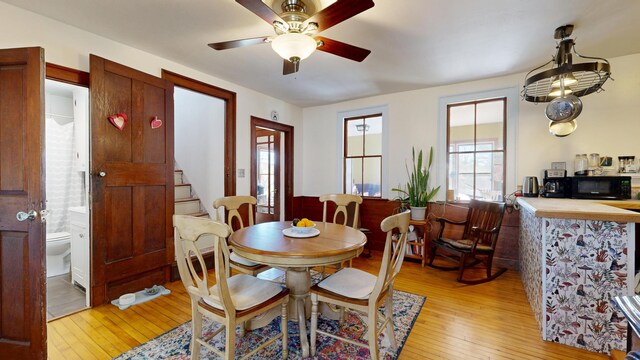 dining space with a ceiling fan, light wood finished floors, and stairway