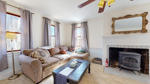 living room with carpet floors, a ceiling fan, baseboards, and a wood stove