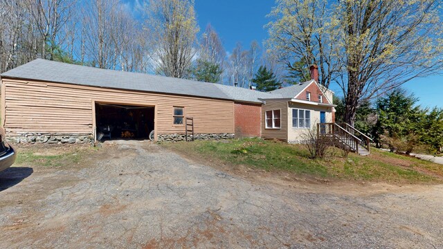 view of home's exterior featuring an outdoor structure, dirt driveway, a chimney, and an attached garage