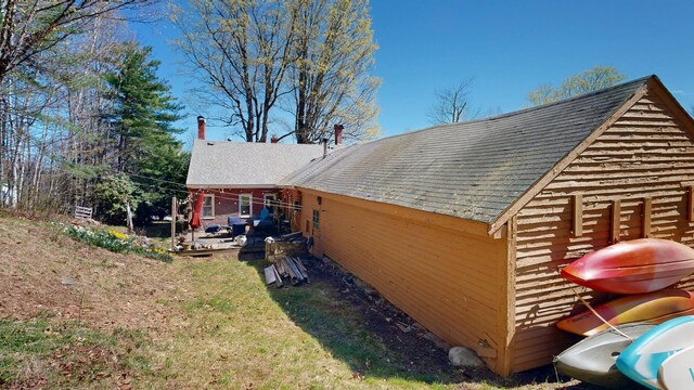 view of side of home featuring a patio, a shingled roof, and a yard